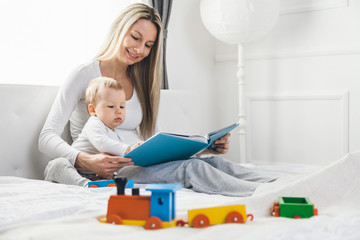 Child education. Happy mother with her toddler sitting on the bed and reading a book