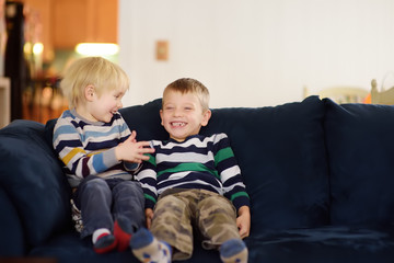 Two cute little boys in striped jumpers talking and laughing sitting on the couch.