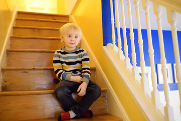 Cute little boy in striped jumper on the stairs at home