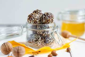 healthy energy granola bites with nuts, dates, honey and sesame in a glass jar on a white table