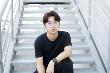 Handsome asian CASUAL glasses man sit on a staircase and smile posing on gray background.  Portrait of young KOREAN against staircase background. © KissShot