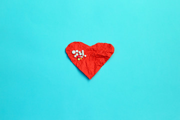 Pills and red crumpled paper heart on blue background. Cardiology concept
