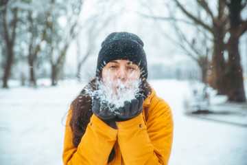 Fototapeta na wymiar woman blowing snow from her hands. snowed park on background. winter season.