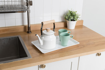 Clean dishes drying on metal dish rack on light background. Kitchen utensils and dishware on wooden shelf. Kitchen interior background.Text space.