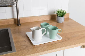 Clean dishes drying on metal dish rack on light background. Kitchen utensils and dishware on wooden shelf. Kitchen interior background.Text space.