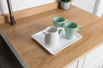 Clean dishes drying on metal dish rack on light background. Kitchen utensils and dishware on wooden shelf. Kitchen interior background.Text space.