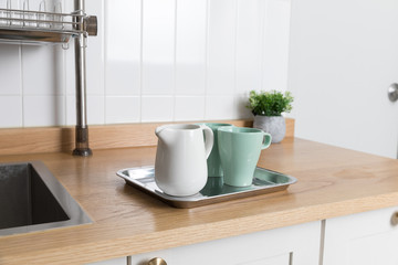 Clean dishes drying on metal dish rack on light background. Kitchen utensils and dishware on wooden shelf. Kitchen interior background.Text space.