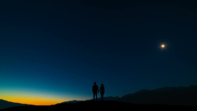 The couple standing on a mountain against a sky with northern light. time lapse