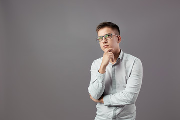 Intelegent guy in glasses dressed in a white shirt is thinking about something on a gray background