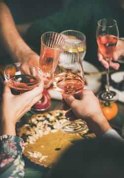 Traditional Christmas or New Year holiday celebration party. Friends or family feasting and clinking glasses with rose wine at festive Christmas table with homemade snacks, vertical composition