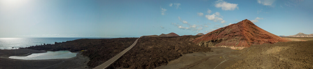 Vista aerea della montagna Bermeja di un color rosso intenso, circondata da campi di lava. Strada costiera che attraversa la lava nera e piccolo lago. Lanzarote, Isole Canarie, Spagna