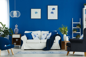 Floral poster on blue wall in chic living room interior with white, blue and wooden furniture in...