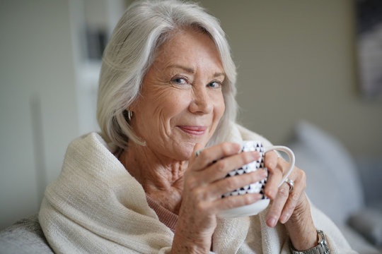  Cosy looking senior woman at home with hot drink