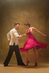 The young dance ballroom couple in gold dress dancing in sensual pose on studio background. Professional dancers dancing tango. Ballroom dance concept. Human emotions - love and passion