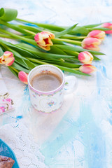 Fototapeta na wymiar A cup of coffee and a bouquet of fresh spring flowers. Tulips. Bright background with blue paints. Free space for text or a postcard.