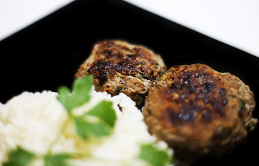 close up of roasted burgers with rice and fresh wet parsley on black plate - food photography