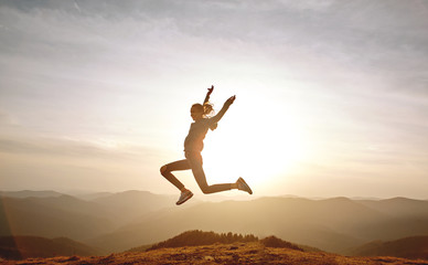 silhouette of Young woman jumping and enjoying life on mountain on sunset sky and mountains background