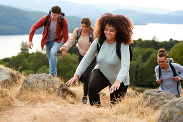 A multi ethnic group of young adult young adult friends smiling while climbing to a mountain summit, close up