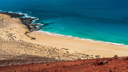 Colorful landscape of red volcanic gravel, white sand and turquoise water. Las Conchas beach as seen from the top of Bermeja Mountain on La Graciosa island, Canary, Spain.