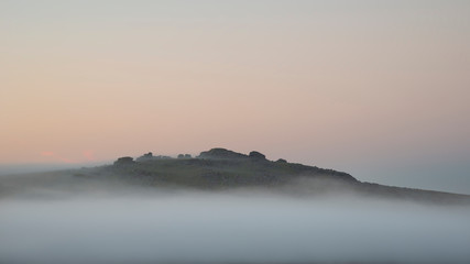Beautiful foggy sunrise landscape over the tors in Dartmoor revealing peaks through the mist