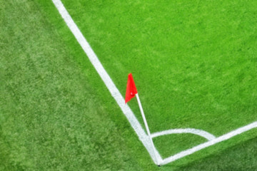 Fototapeta premium Blurry of green soccer field.Beautiful grass on the stadium.Abstract football ground background with white stripe line and red flag on the corner.Background,Sport,Texture Concept