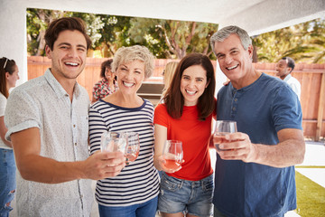 Parents and adult children raise glasses to camera in garden