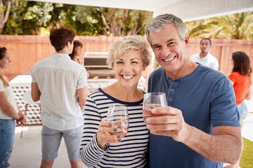 Senior couple at a backyard party raising glasses to camera