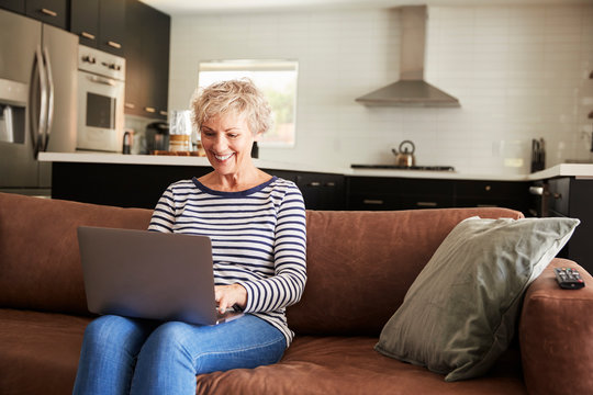 Senior white woman sitting on couch using laptop computer