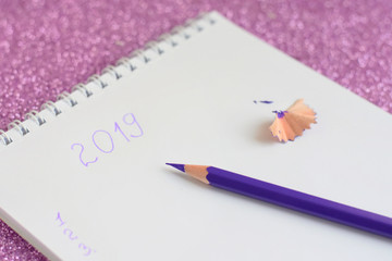 New year 2019 to do list with selective focus in spiral white paper album. color violet pencil and notebook on shiny sparkle glittery background. back to school.