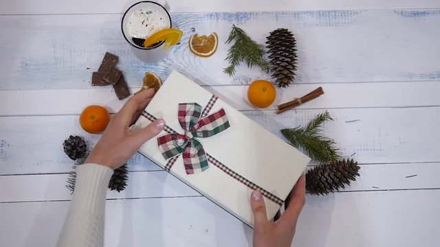 Plan from top to bottom. Fully visible table with decorations. Women's hands open a Christmas present