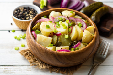 Potato salad with pickled cucumbers and onion in bowl on white wooden table. Selective focus.
