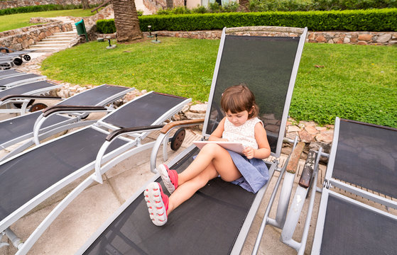 little girl with a tablet sitting on a lounger