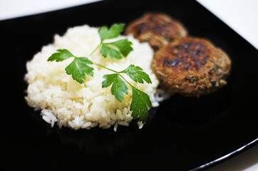 roasted burgers with rice and fresh wet parsley on black plate - food photography