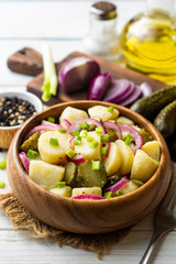 Potato salad with pickled cucumbers and onion in bowl on white wooden table. Selective focus.