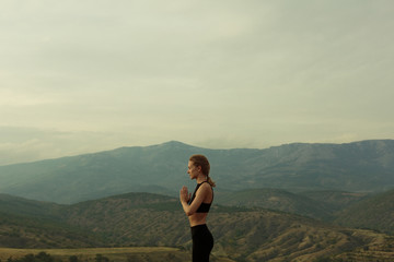 Naklejka na ściany i meble Profile portrait of slim girl dressed in black sport outfit, black top, meditating, praying, closed eyes, staying in the mountains