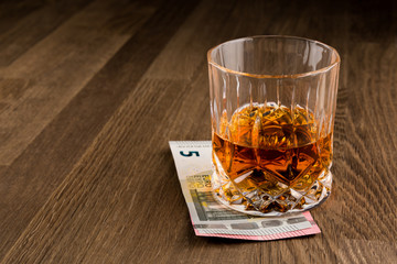 Whiskey Glass over Euro banknotes isolated on Wooden Table. Copy Space