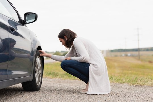 Woman checking car tyre during breakdown