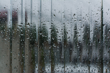 window glass with dripping raindrops and blurred background