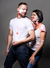 Beautiful couple of artists wearing jeans and white t-shirts soiled with white and red paint posing on gray. Palm prints painted on their faces. Conceptual, fashion, lifestyle design