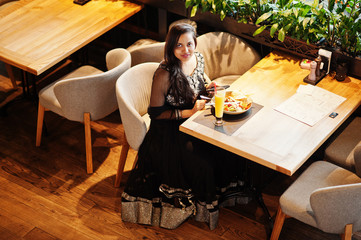 Pretty indian girl in black saree dress posed at restaurant, sitting at table with juice and salad....