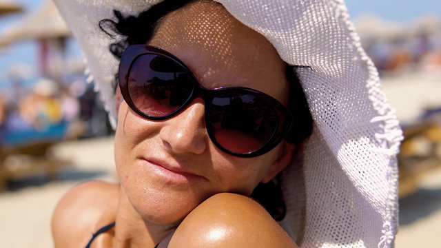 Beautiful woman on beach wear straw hat and glasses protection, look at distance and smile with blurred umbrelas at background