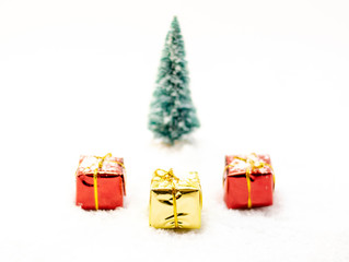 Three presents, two red and one yellow with ribbons isolated on white, Christmas tree in the background.