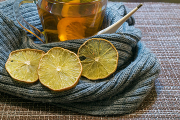A Cup of tea with lemon wrapped in a soft gray scarf. Dried lemon wedges.