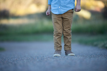 Pair of kids feet wearing leather shoes on field. Little boy wearing beige trousers and brown leather shoes staying on sand