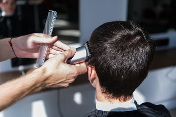 Perfect trim. Rear view close-up of young man getting haircut by hairdresser with electric razor.