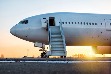 Fototapeta na wymiar White wide-body passenger aircraft with a boarding steps at the airport apron in the evening sun