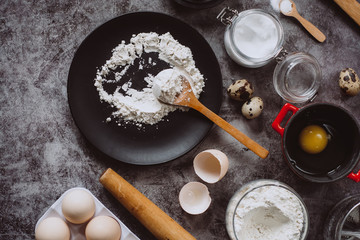 Ingredients and utensils for baking. Spoon with flour, dishes, eggs,  butter salt and rolling pin on a grey background. Flat lay. Text space