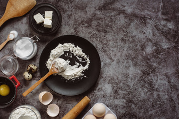Obraz na płótnie Canvas Ingredients and utensils for baking. Spoon with flour, dishes, eggs, butter salt and rolling pin on a grey background. Flat lay. Text space