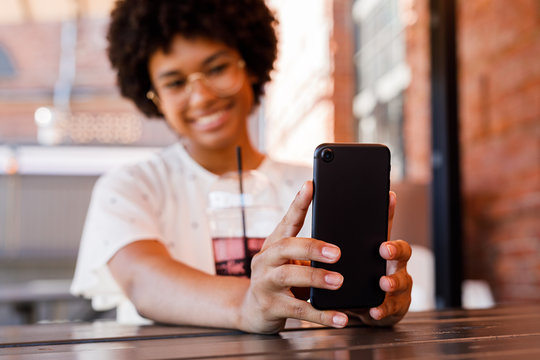 Close up of woman hands holding a smartphone. Young blogger taking selfie with a drink on table.