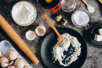 Ingredients and utensils for baking. Spoon with flour, dishes, eggs,  butter salt and rolling pin on a grey background. Flat lay. 